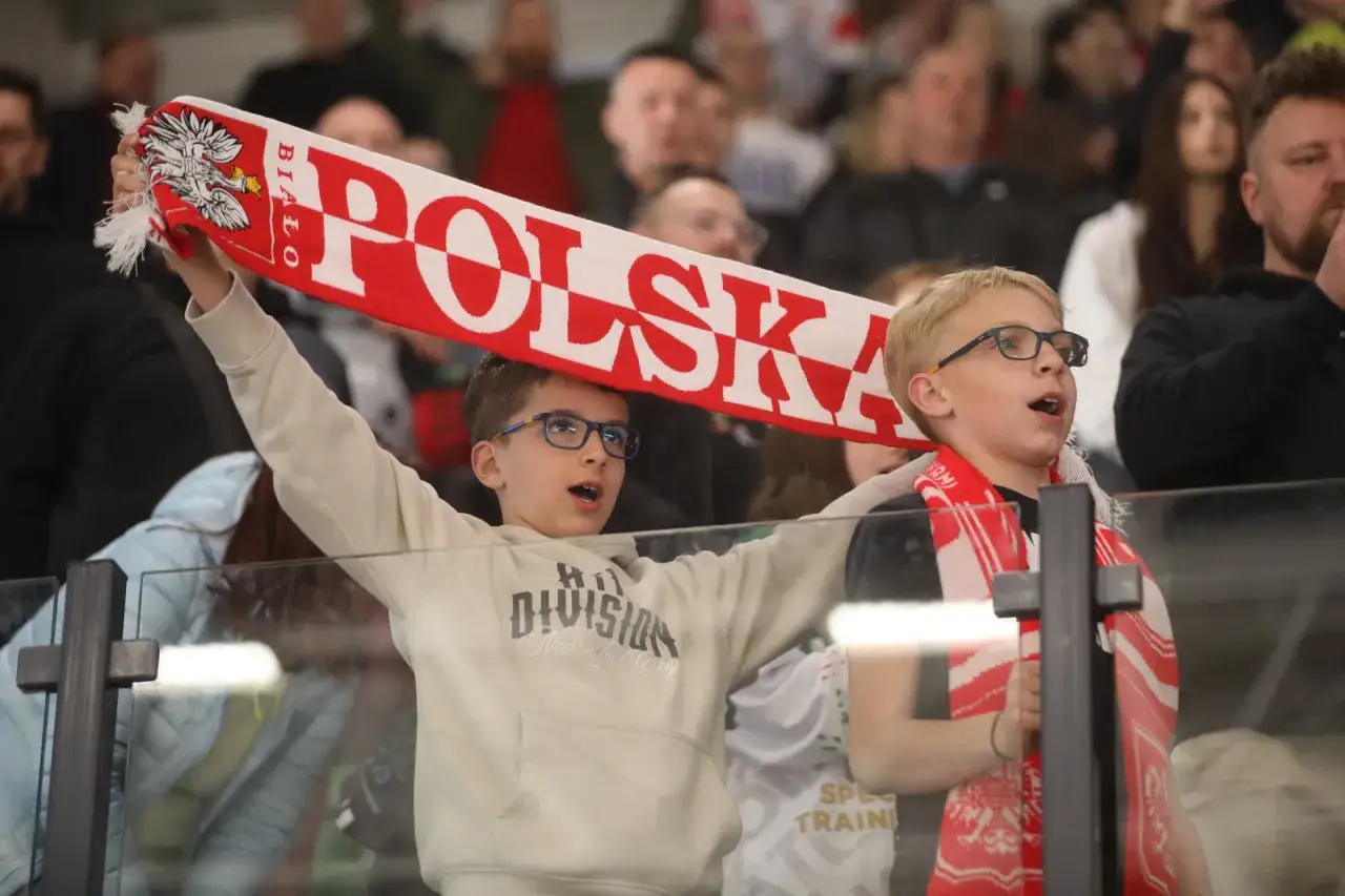 Dw&oacute;ch chłopc&oacute;w kibicuje, trzymając biało-czerwoną flagę z napisem 