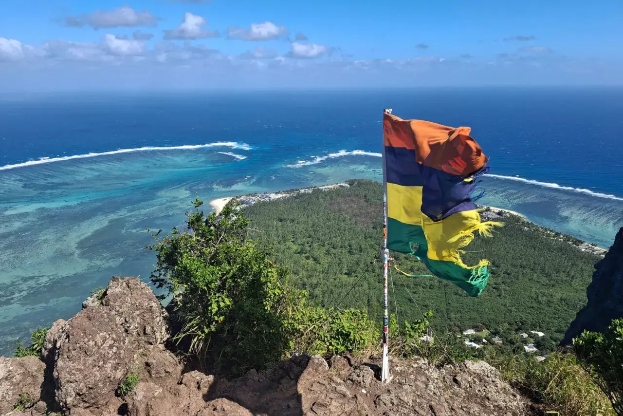 En flagga vajar p&aring; toppen av Le Morne, med en fantastisk utsikt &ouml;ver turkost hav och frodig gr&ouml;nska.