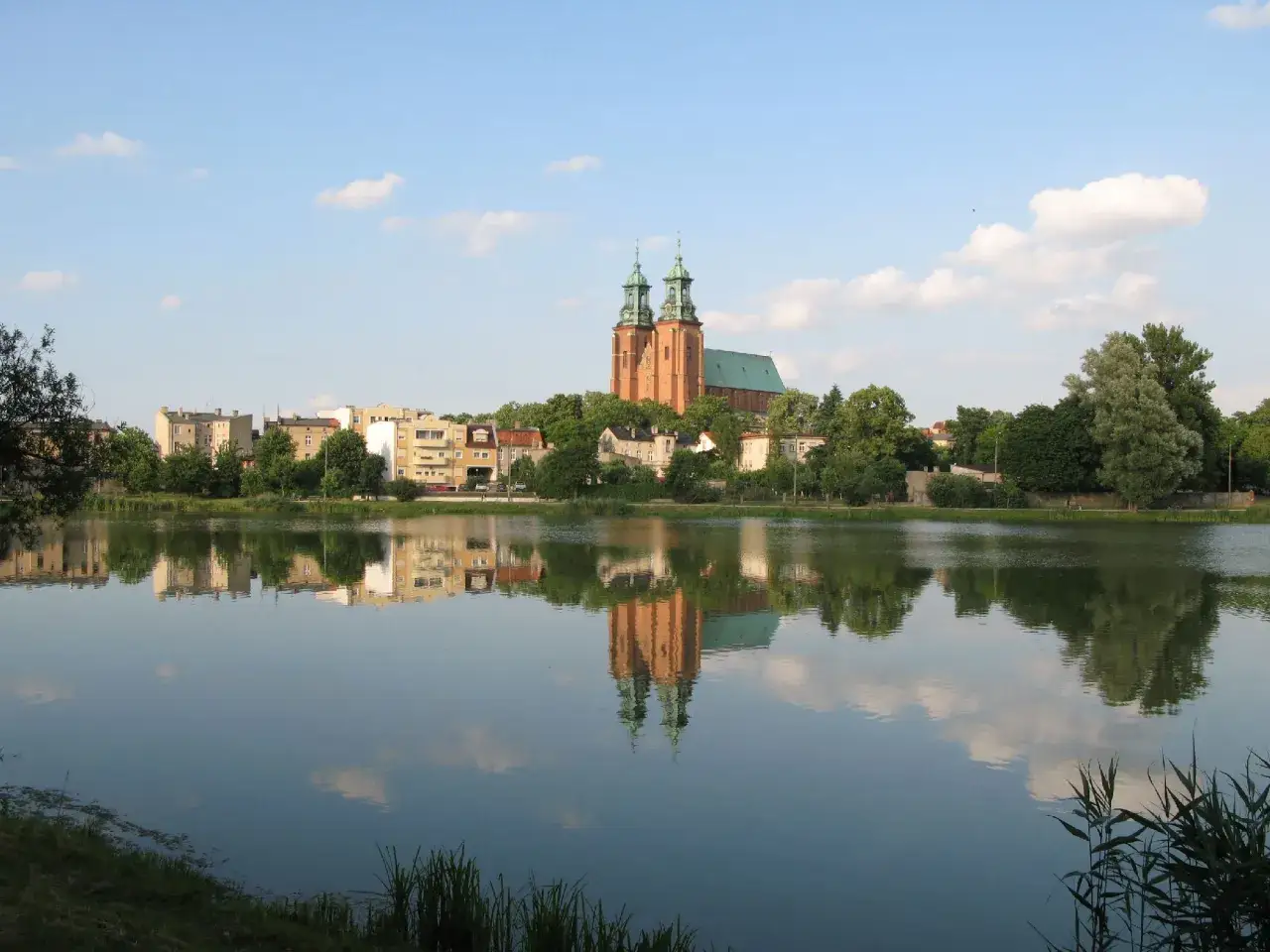 Gniezno jezioro z odbiciem katedry i miasta w spokojnej tafli wody.
