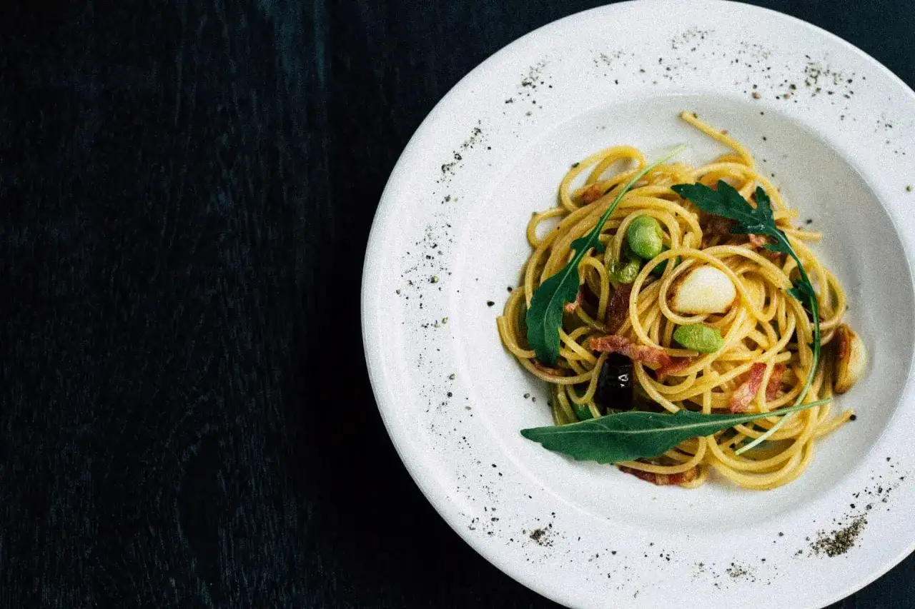 Une assiette de spaghetti avec des fèves, du lard et de la roquette. Une belle idée recette pâtes pour un repas simple et savoureux.