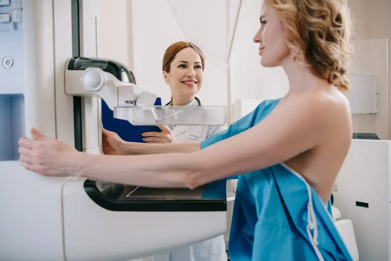 Kobieta przygotowuje się do mammografii, uśmiechnięta lekarka asystuje przy aparacie.