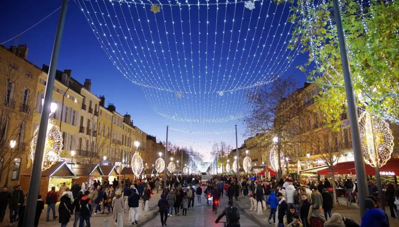 Foule joyeuse au march&eacute; de no&euml;l Vaucluse, illumin&eacute; par des guirlandes scintillantes et des d&eacute;corations festives.