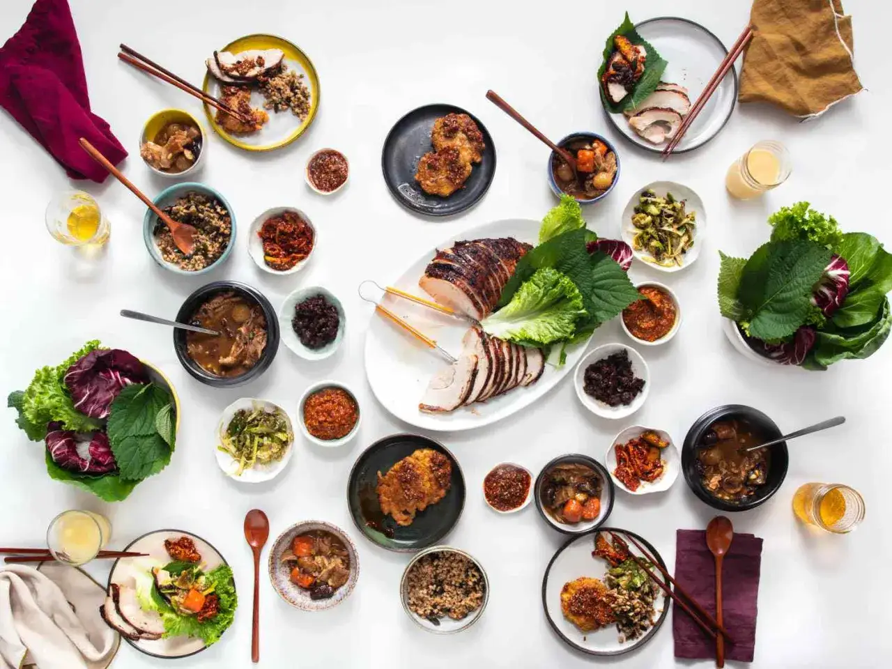 Obficie zastawiony stół z koreańskimi banchan: mięso, warzywa, ryż i sosy.