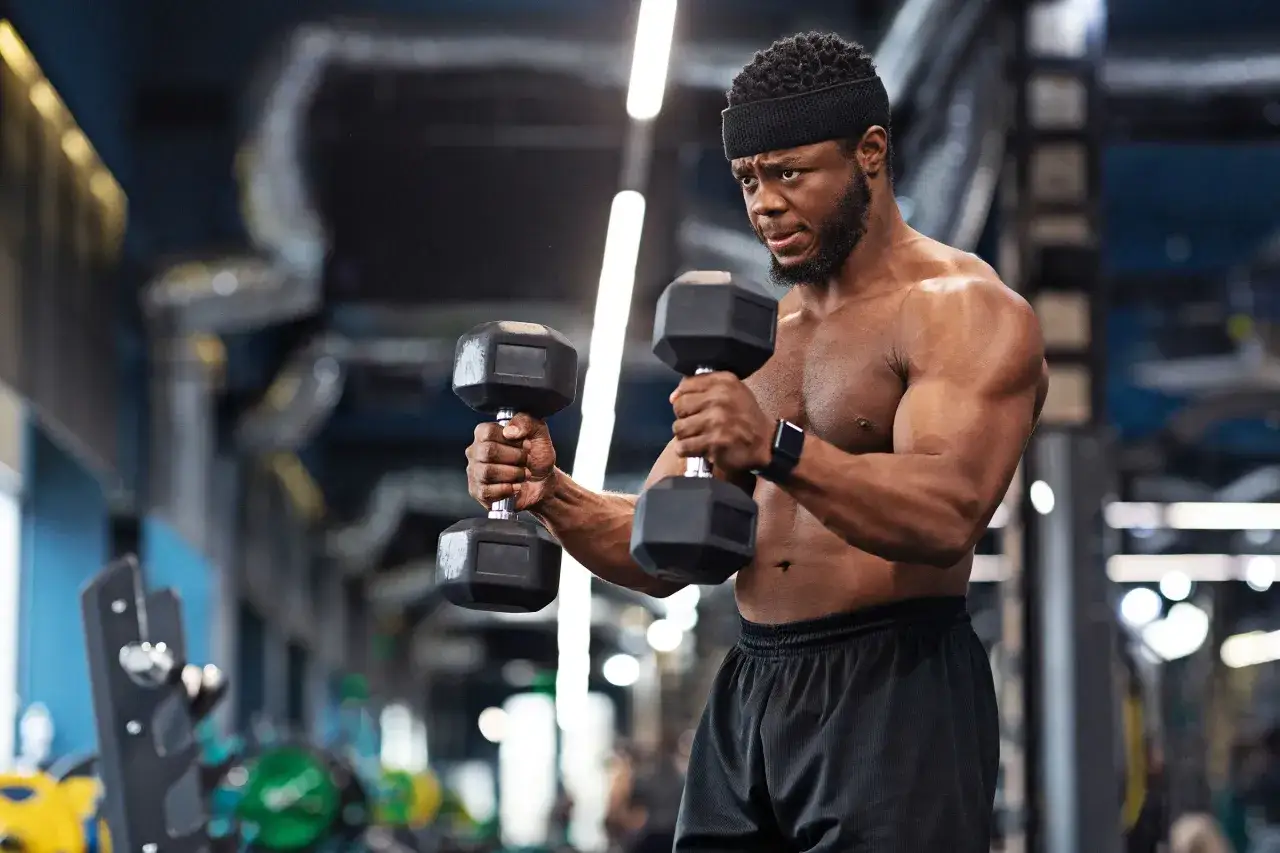 Mężczyzna wykonuje ćwiczenie hammer curl z hantlami, skupiony na treningu bicepsów w siłowni.