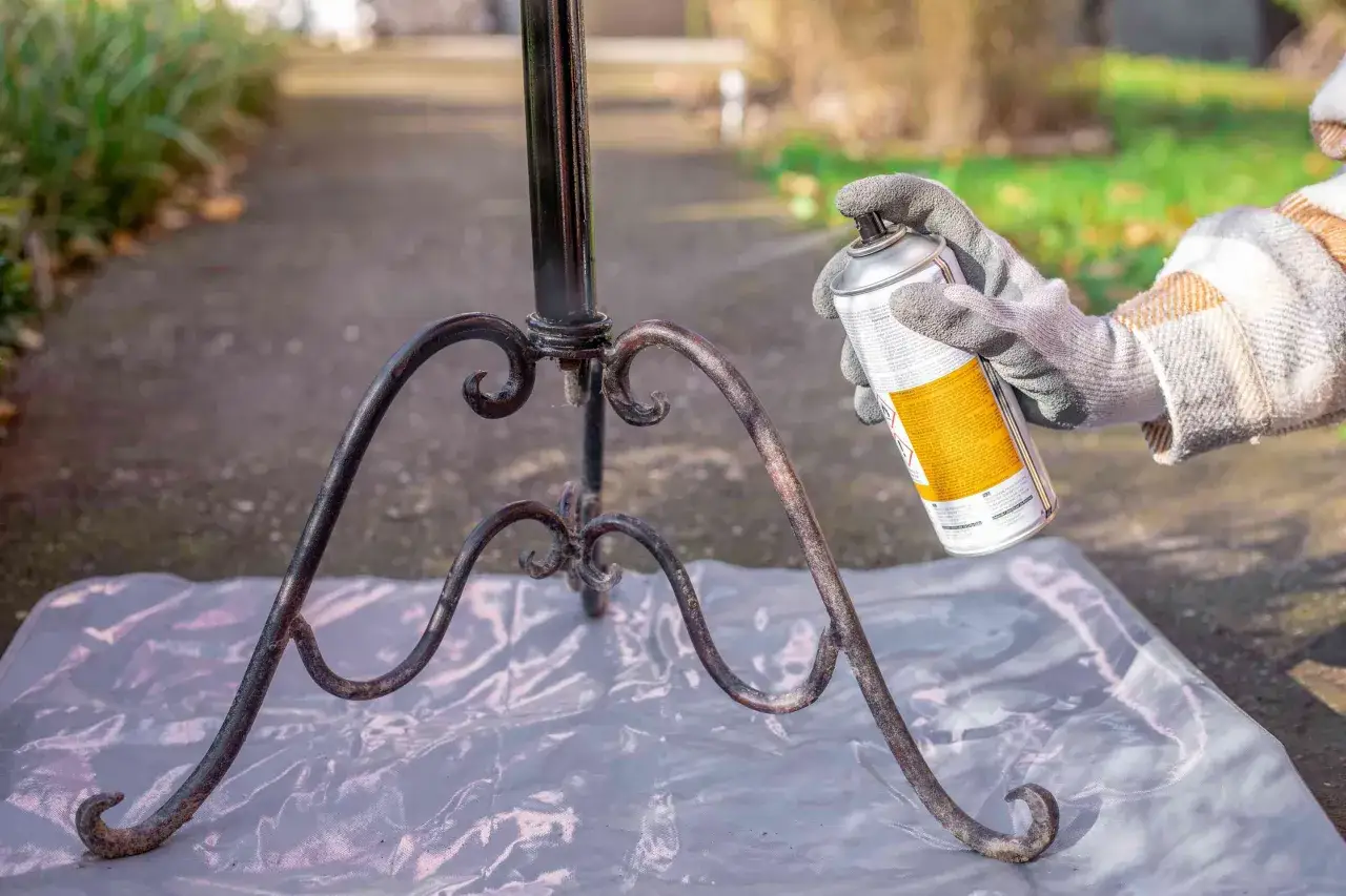 En hand med handske sprayar en rostig metallställning utomhus.