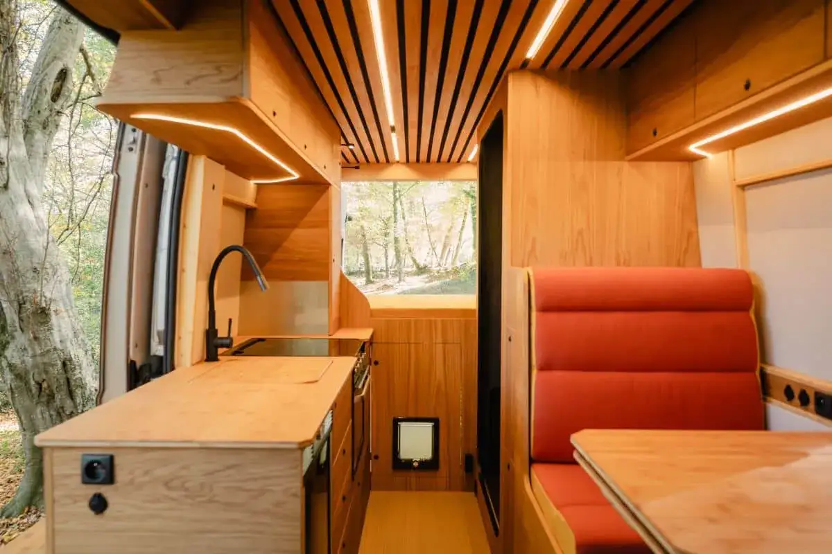 Aménagement camping-car pour chien : cuisine en bois, banquette rouge et fenêtre sur la nature. Un espace cosy pour voyager avec son compagnon.