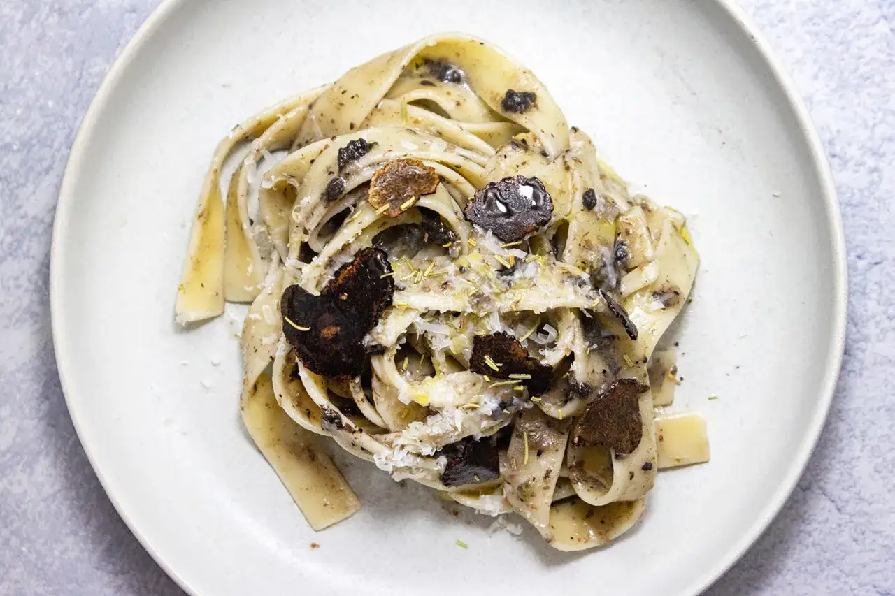 Tagliatelle z truflami, posypane parmezanem i ziołami. Luksusowy makaron z truflami na talerzu.