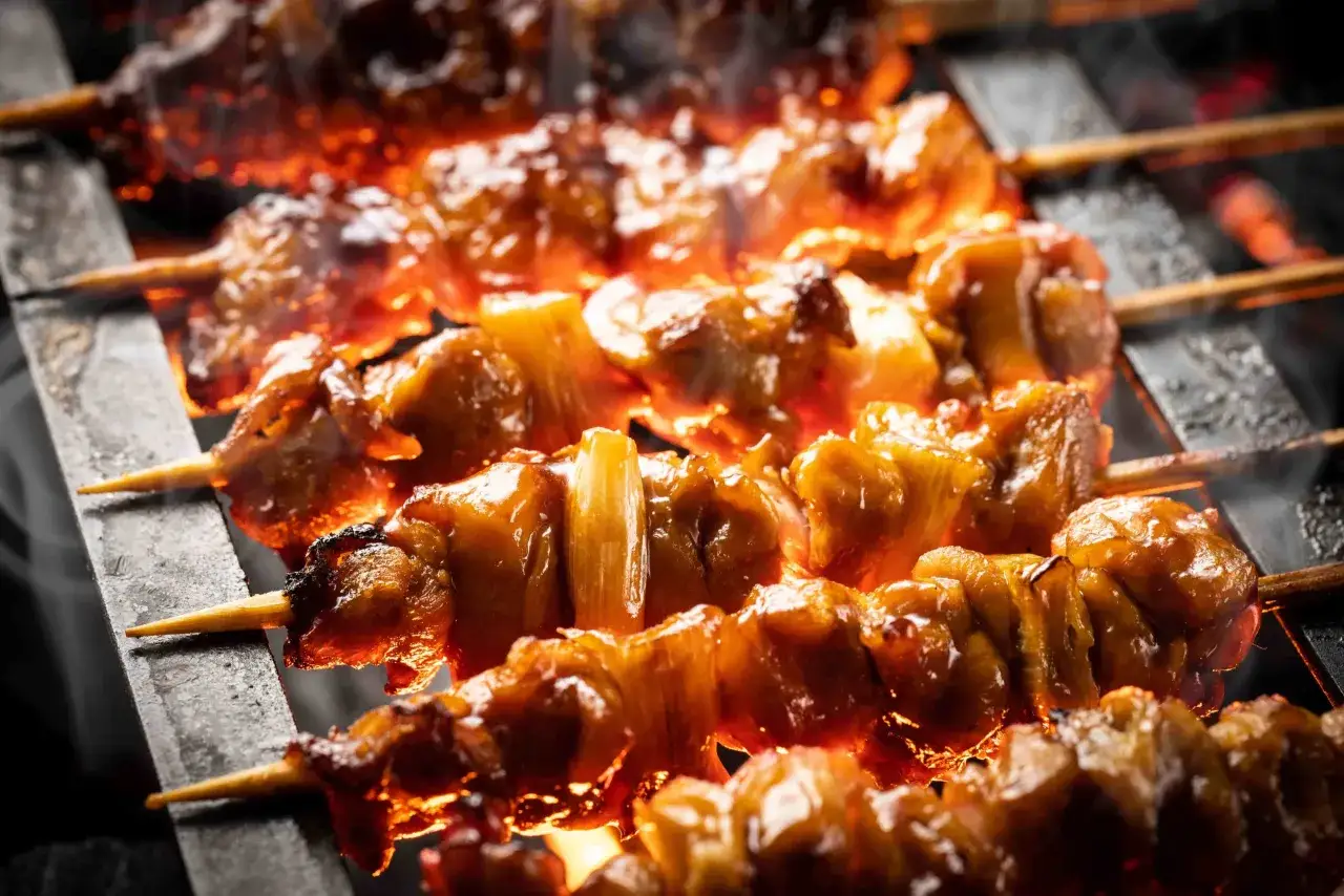 Brochettes de bœuf et fromage grillées sur un feu vif, dégageant une fumée alléchante.