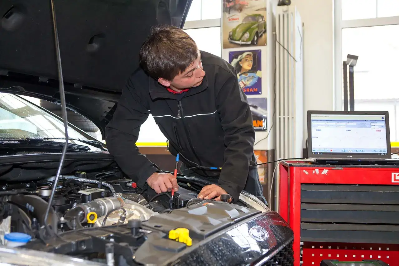 Mechaniker prüft Motor, da das Auto nicht mehr richtig beschleunigt. Diagnosegerät und Laptop sind angeschlossen.