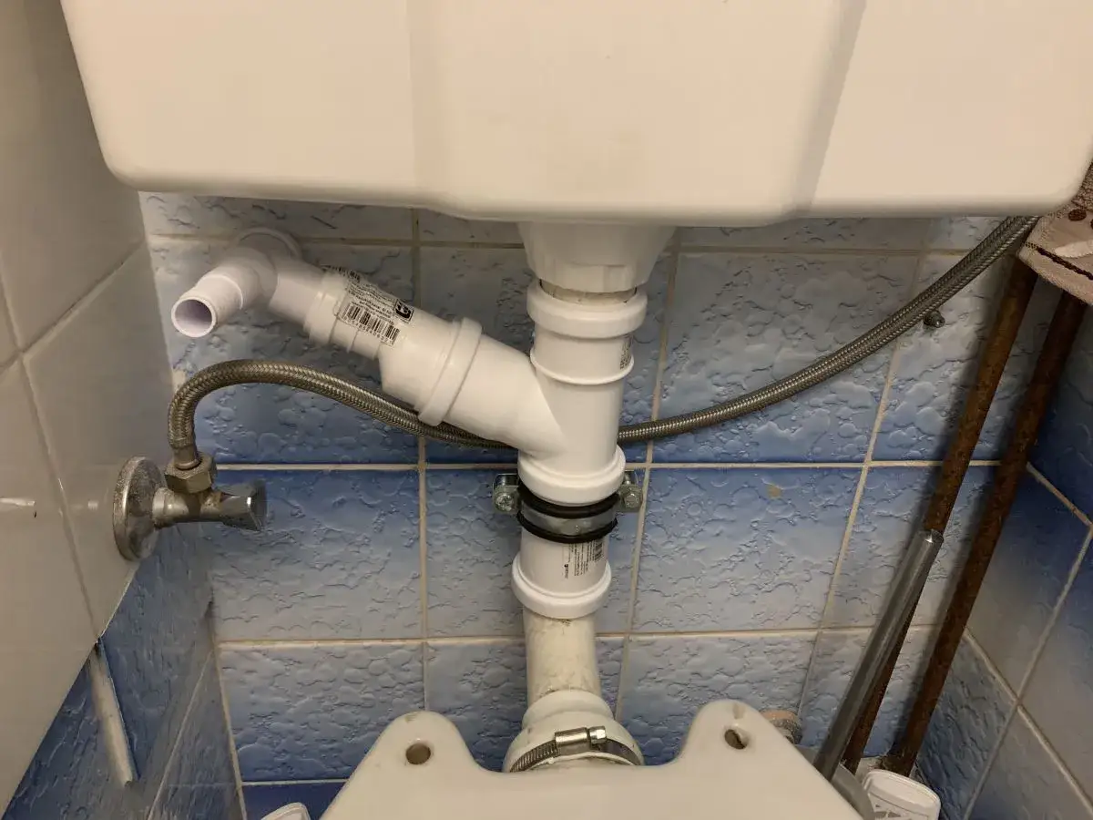 Nowa instalacja do podłączenia pralki do odpływu. Białe rury PCV łączą się z odpływem pod toaletą.