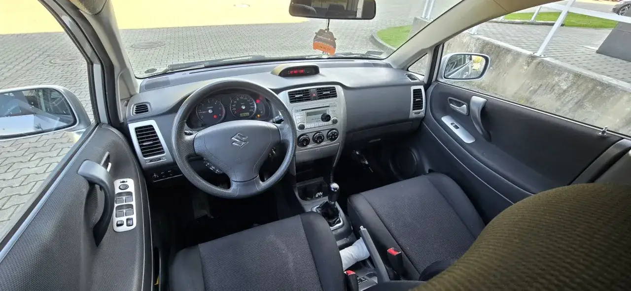 Wnętrze Suzuki Liana: kierownica z logo, deska rozdzielcza z radiem i zegarami, czarne fotele.