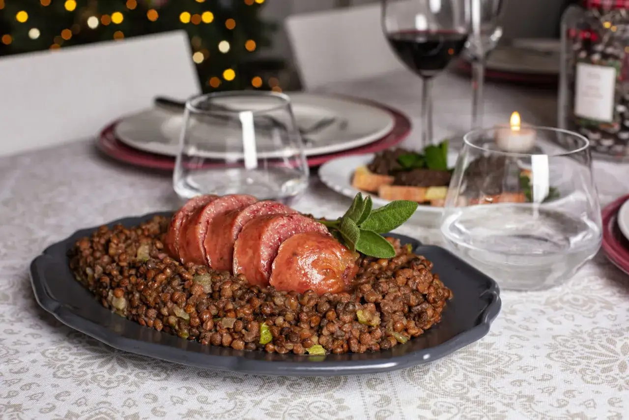 Piatto di cotechino affettato su lenticchie, pronto per essere abbinato a un vino rosso corposo.