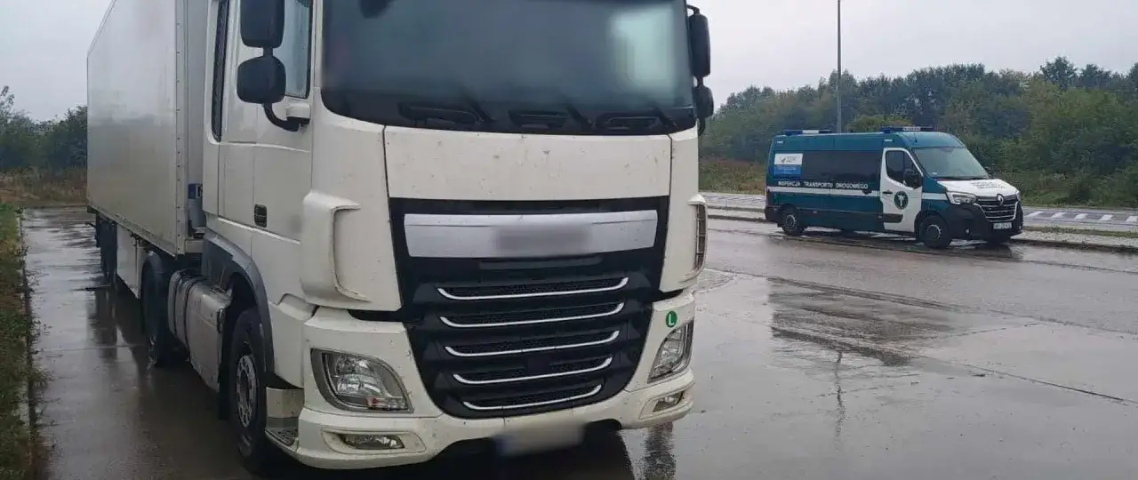 Biała ciężarówka i zielono-biały bus Inspekcji Transportu Drogowego na mokrej drodze. Kierowca ciężarówki otrzymał zgłoszenie.