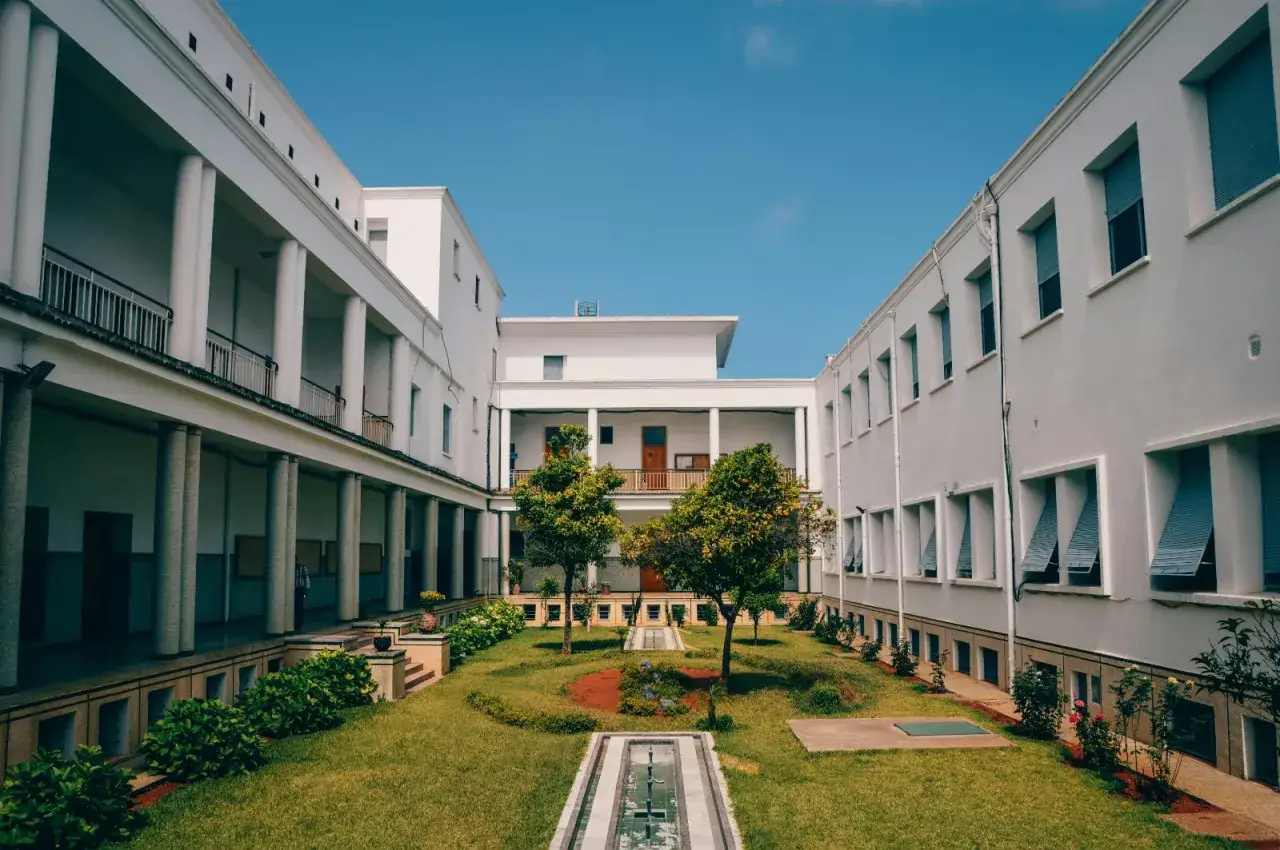 Cour intérieure d'un bâtiment blanc, idéale pour un étudiant français cherchant une aide au logement en Espagne. Jardin verdoyant et ciel bleu.