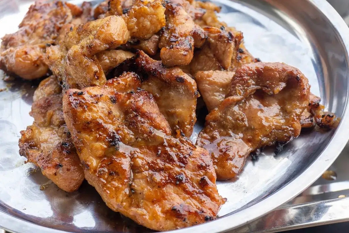 Soczysta karkówka w marynacie, grillowana do perfekcji, lśni na metalowej tacy. Aromatyczny zapach zachęca do spróbowania.