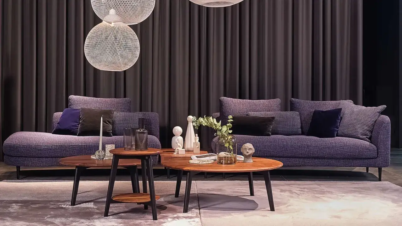 Lila Sofas mit Kissen und Holztischen. Dunkle Vorhänge im Hintergrund. Welche Farbe passt zu Lila? Hier sind einige Ideen für Ihr Zuhause.