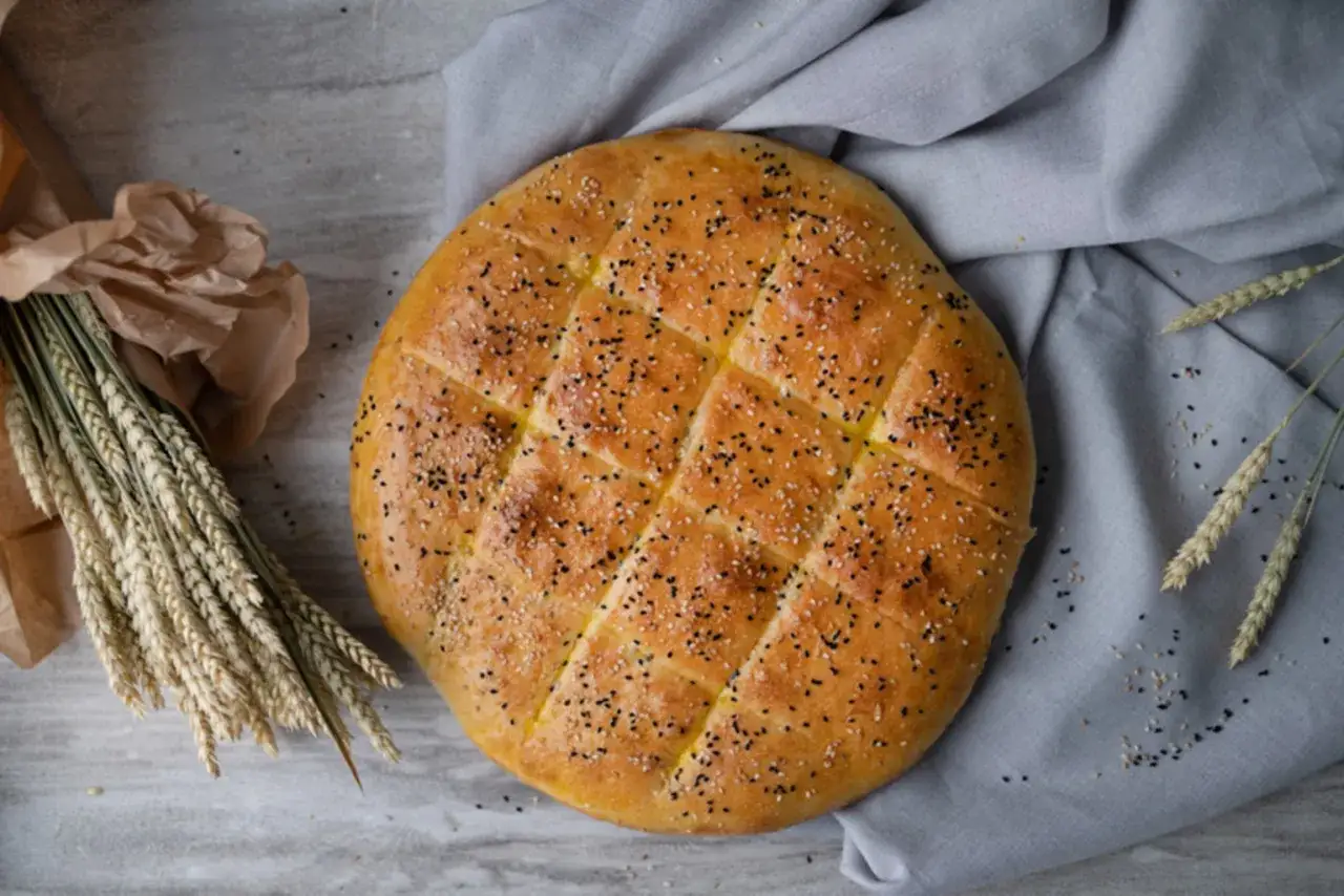 Goldbraunes Fladenbrot, bestreut mit Sesam und Schwarzkümmel, wartet auf sein Fladenbrot Rezept. Daneben liegen Ähren.