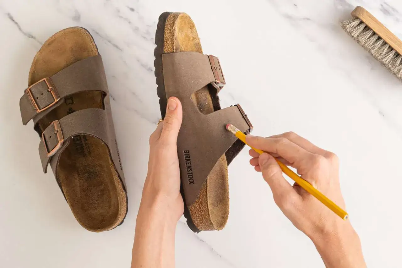 Come si lavano le Birkenstock: una mano usa una gomma da matita per pulire una ciabatta marrone.