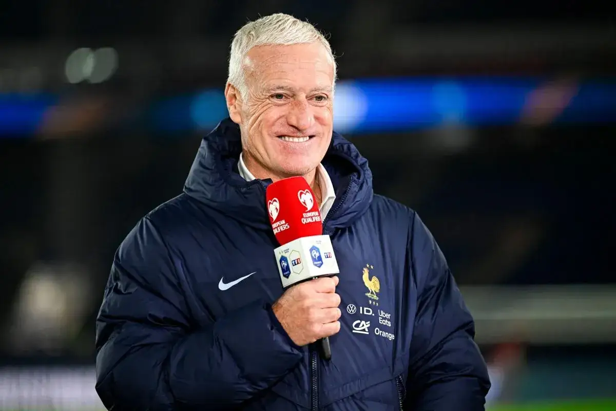 Uśmiechnięty Didier Deschamps, trener Francji, trzyma mikrofon podczas wywiadu.
