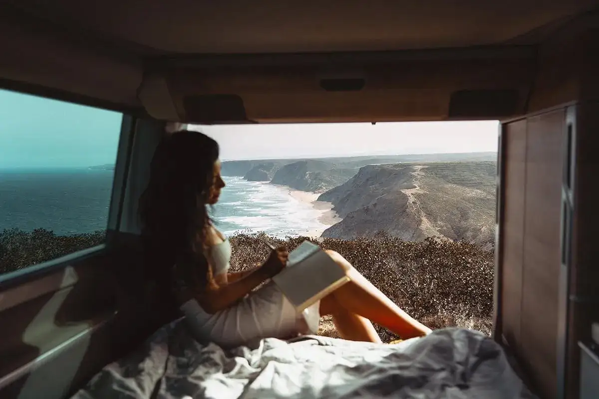 Frauen-Silhouette liest Buch in einem Camper mit Blick auf die K&uuml;ste Portugals. Perfekt f&uuml;r die beste Reisezeit Portugal Klimatabelle.