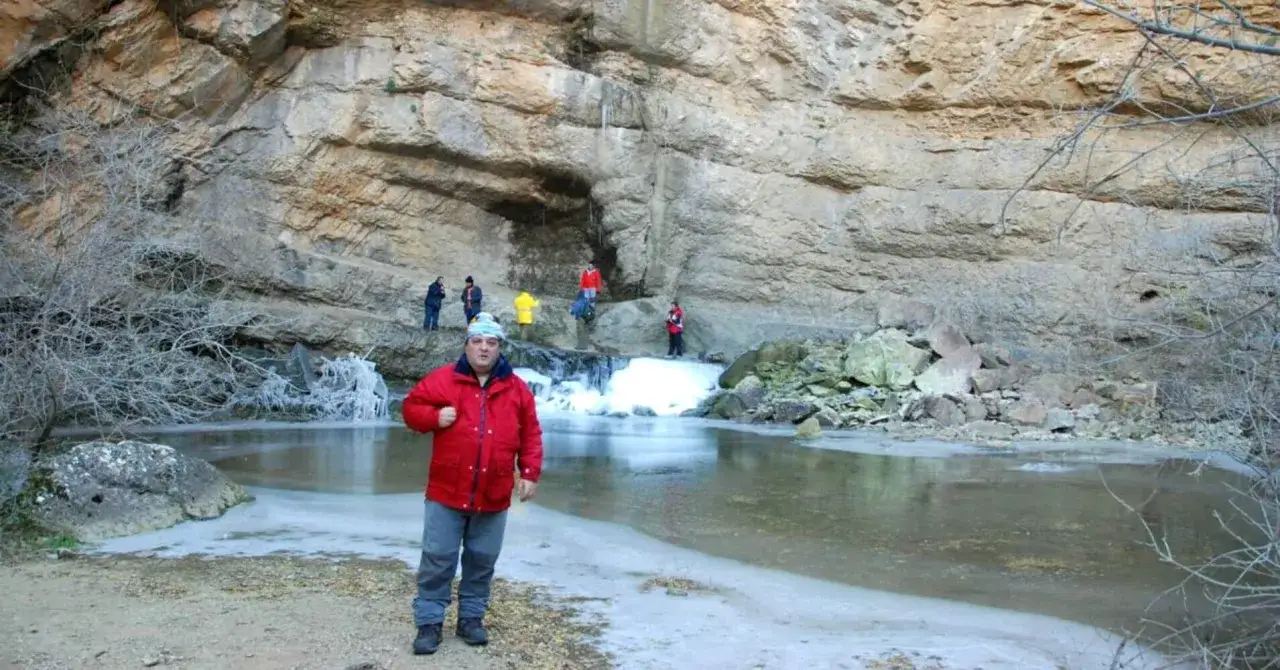 Un hombre con chaqueta roja posa frente a la cascada del gollorio, con hielo y rocas alrededor.