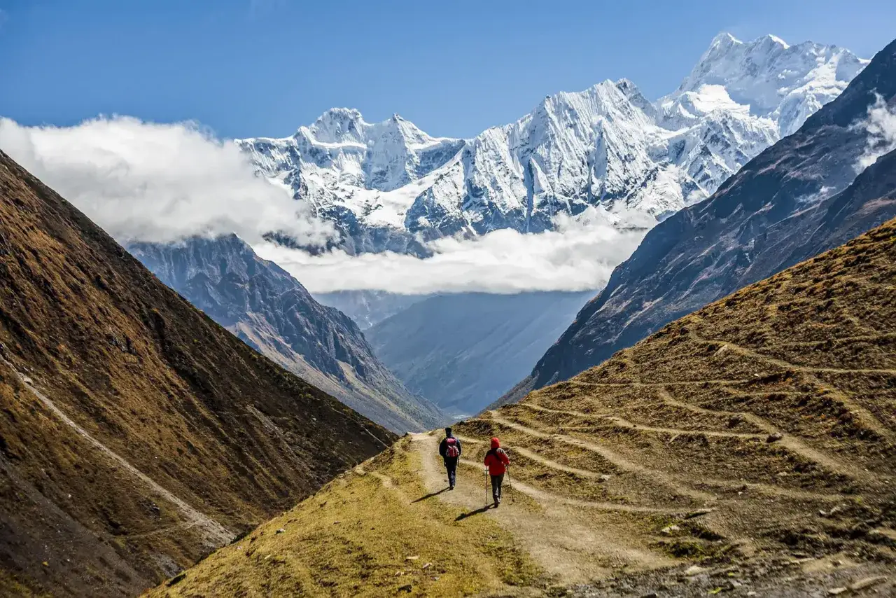 Dwie osoby wędrujące ścieżką w dolinie, z majestatycznymi, ośnieżonymi szczytami Himalajów w tle. Niezapomniany nepal trekking.