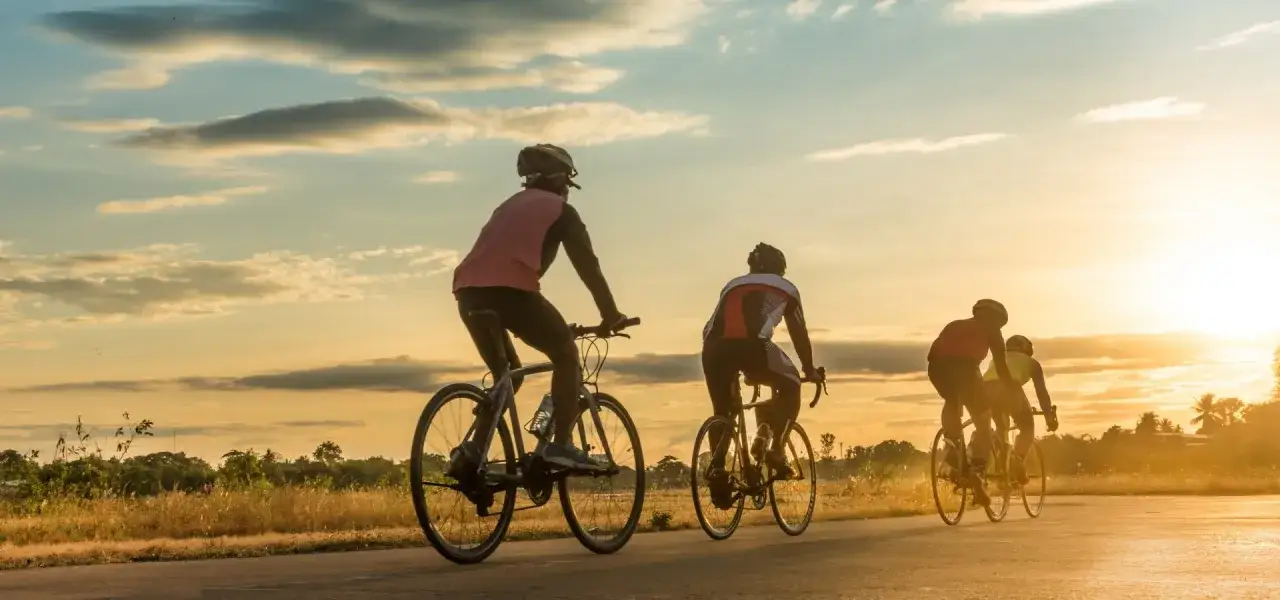 Grupa rowerzystów przemierza malowniczy bursztynowy szlak rowerowy o zachodzie słońca.