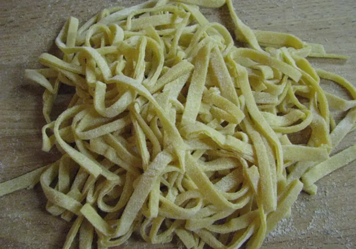 Świeży, domowy makaron, jak z przepisu babci, ułożony na drewnianym blacie.