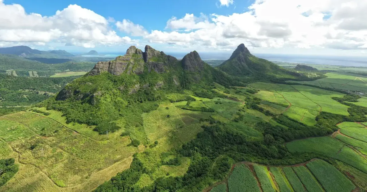 Górzyste krajobrazy Mauritiusa, bujna zieleń pól i lasów, chmury na niebie. To piękny widok, który może towarzyszyć nam podczas deszczowej pory na Mauritiusie.