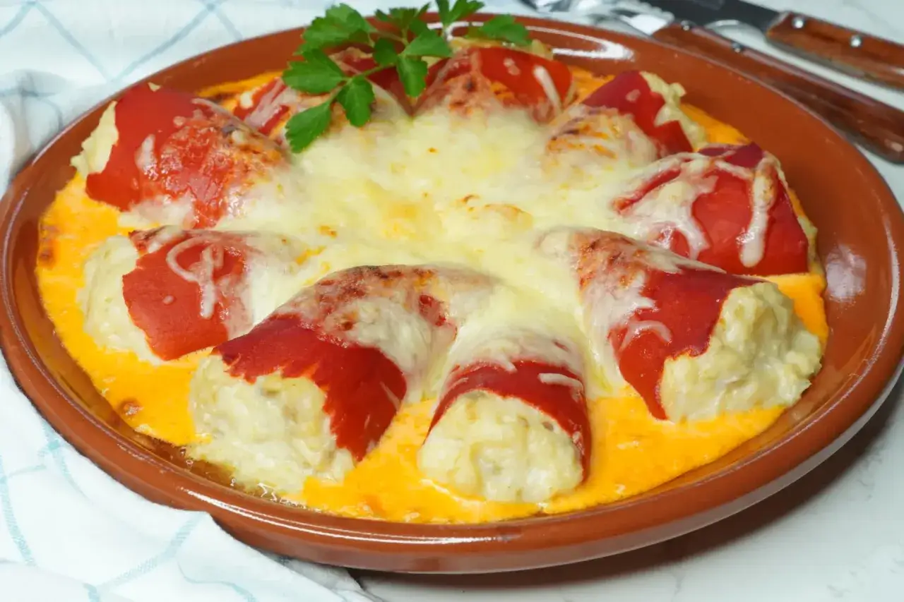 Pimientos rellenos de bacalao gratinados con queso, servidos en una cazuela de barro.