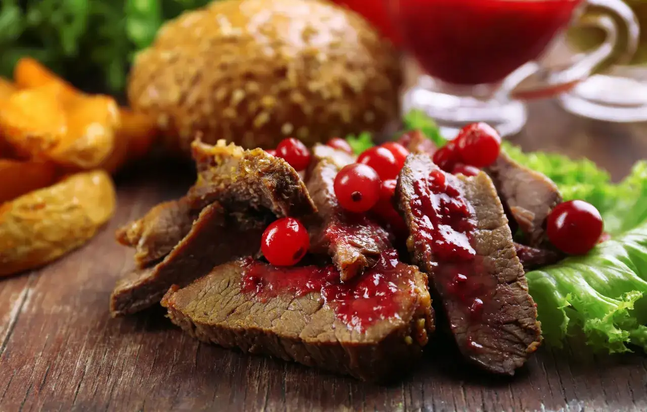Schmackhafter Hirschbraten geschmort, serviert mit roten Beeren und Kartoffelspalten. Ein köstliches Rezept für Genießer.