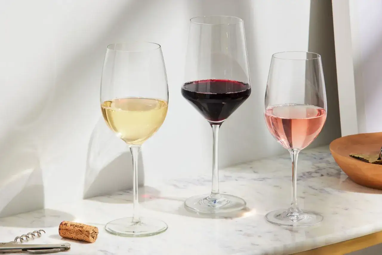 Drei Weingl&auml;ser mit Wei&szlig;-, Rot- und Ros&eacute;wein stehen bereit f&uuml;r eine Wein-Bewertung. Ein Korkenzieher und ein Korken liegen daneben.