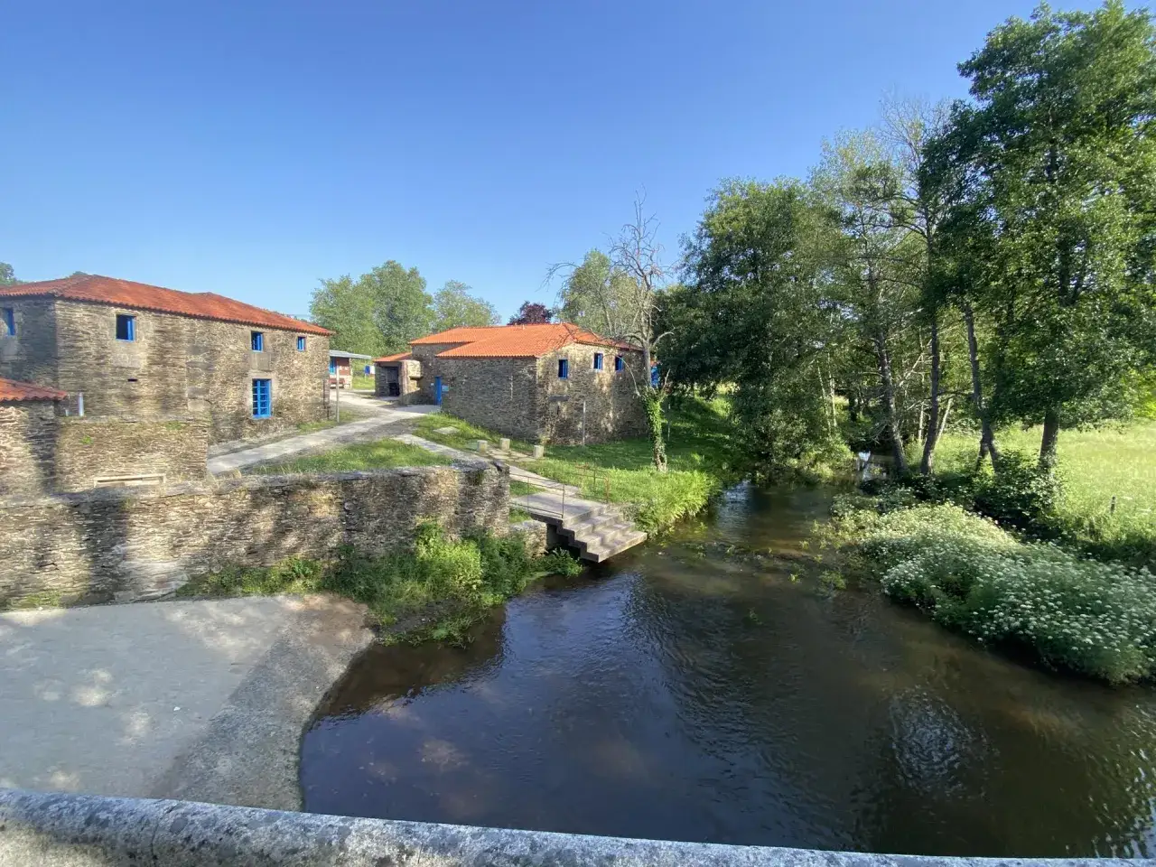 Casas de piedra con tejados rojos y ventanas azules junto a un río. Un lugar idílico que ver en Vila de Cruces.