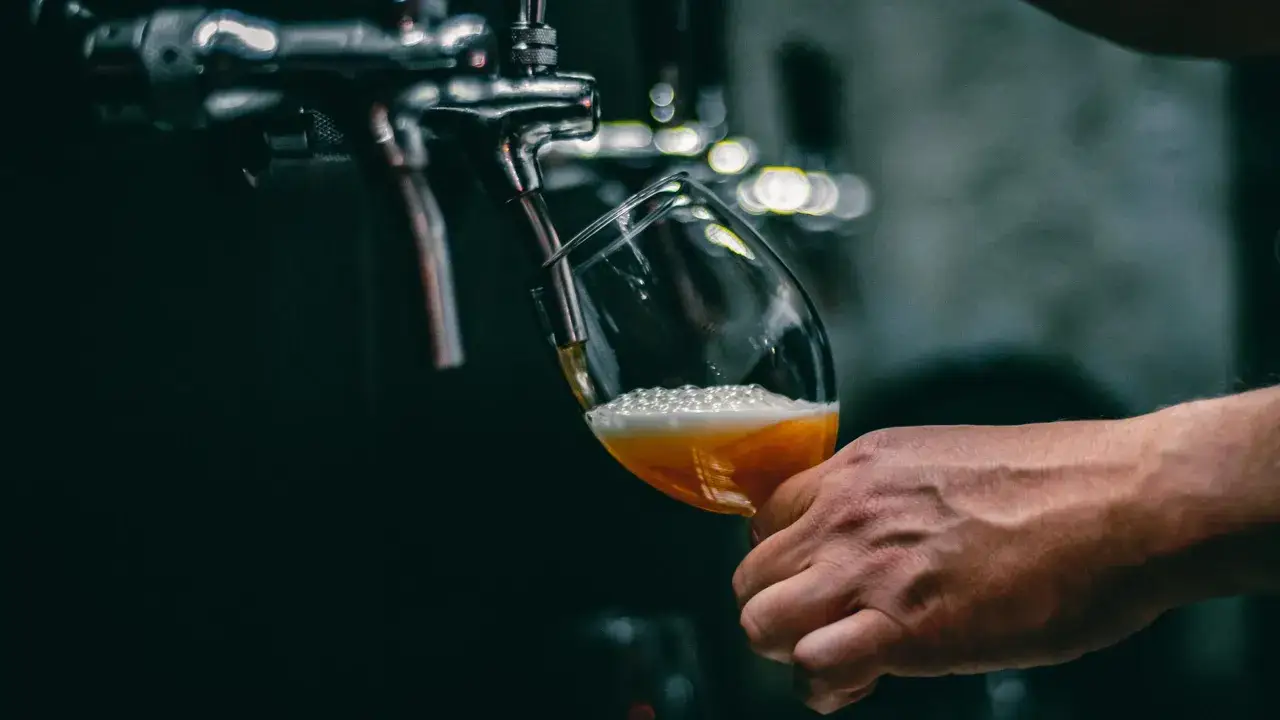 Mano che versa una birra ghiacciata da un rubinetto in un bicchiere, con schiuma abbondante.