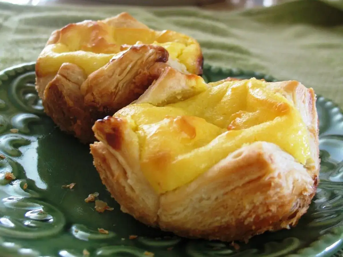 Zwei goldbraune Pastéis de Nata mit cremigem Vanillepudding-Füllung auf einem grünen Teller. Ein köstliches pastéis de nata rezept vanillepudding.
