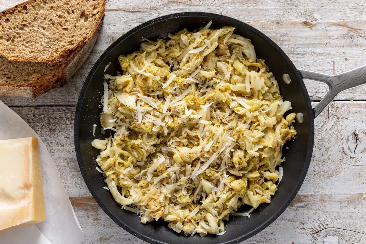 Verza in padella, saporita e profumata, cosparsa di formaggio grattugiato, accanto a pane rustico e un pezzo di formaggio.