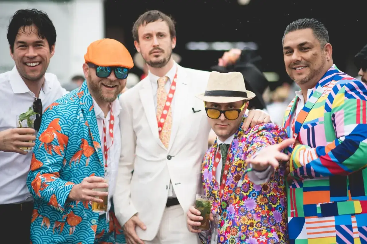 Men at the Kentucky Derby wear bold, colorful suits. One sports a goldfish-patterned jacket, another a floral one, and a third a geometric design.
