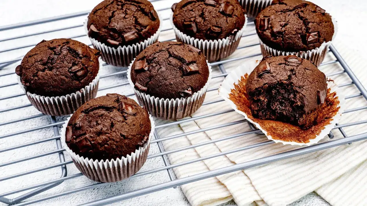 Schokoladenmuffins mit Schokostückchen auf einem Gitter. Ein Muffin ist angeknabbert und zeigt das saftige Innere. Perfekt für ein schnelles Muffins Rezept.