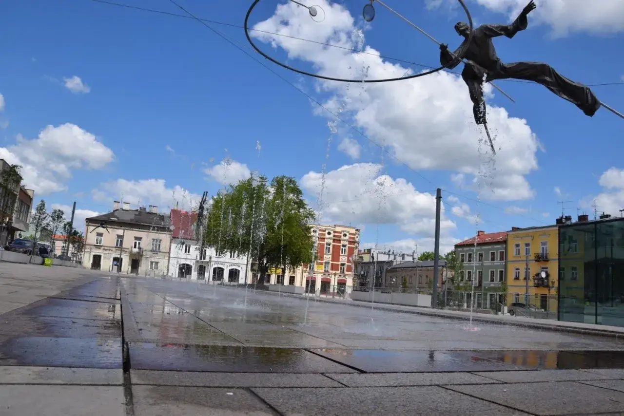Radosny rynek Częstochowa z fontanną i rzeźbą akrobaty na tle kolorowych kamienic.