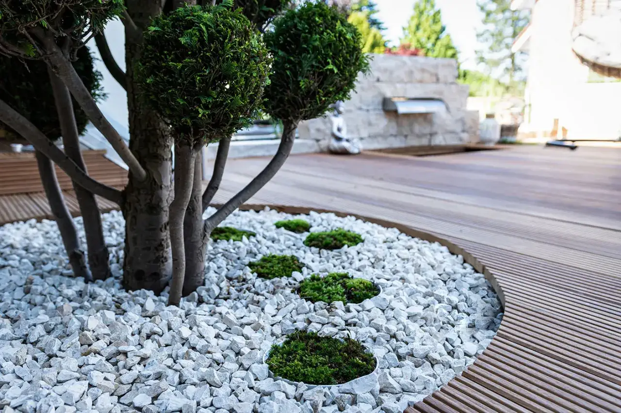 Moderner **Garten ohne Rasen** mit Kiesbeet, Moosinseln und kunstvoll geschnittenen B&auml;umen. Eine Holzterrasse grenzt den Bereich ab.