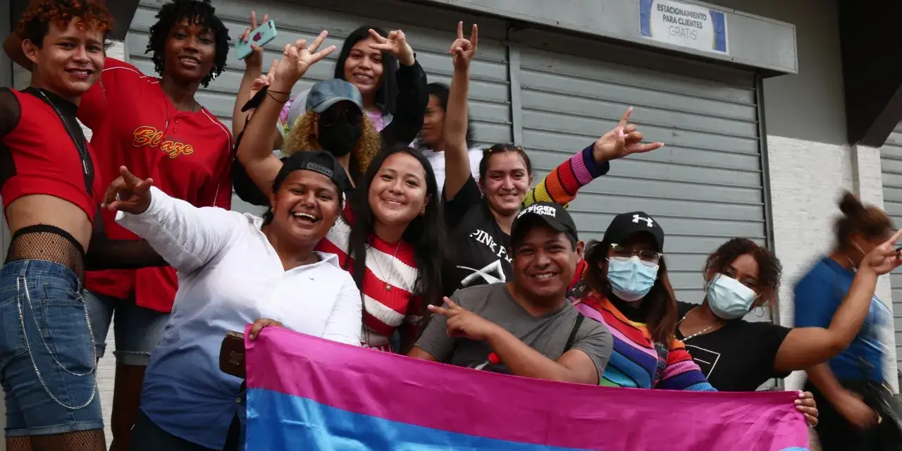 A group of smiling people, some holding a bisexual flag, celebrate in Honduras.
