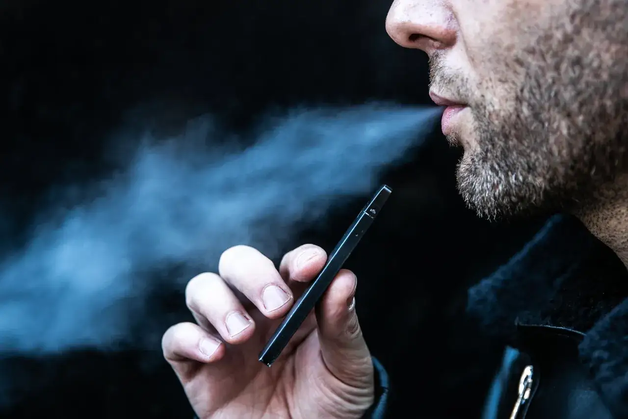 Hombre exhalando vapor de un vapeador para dejar de fumar.