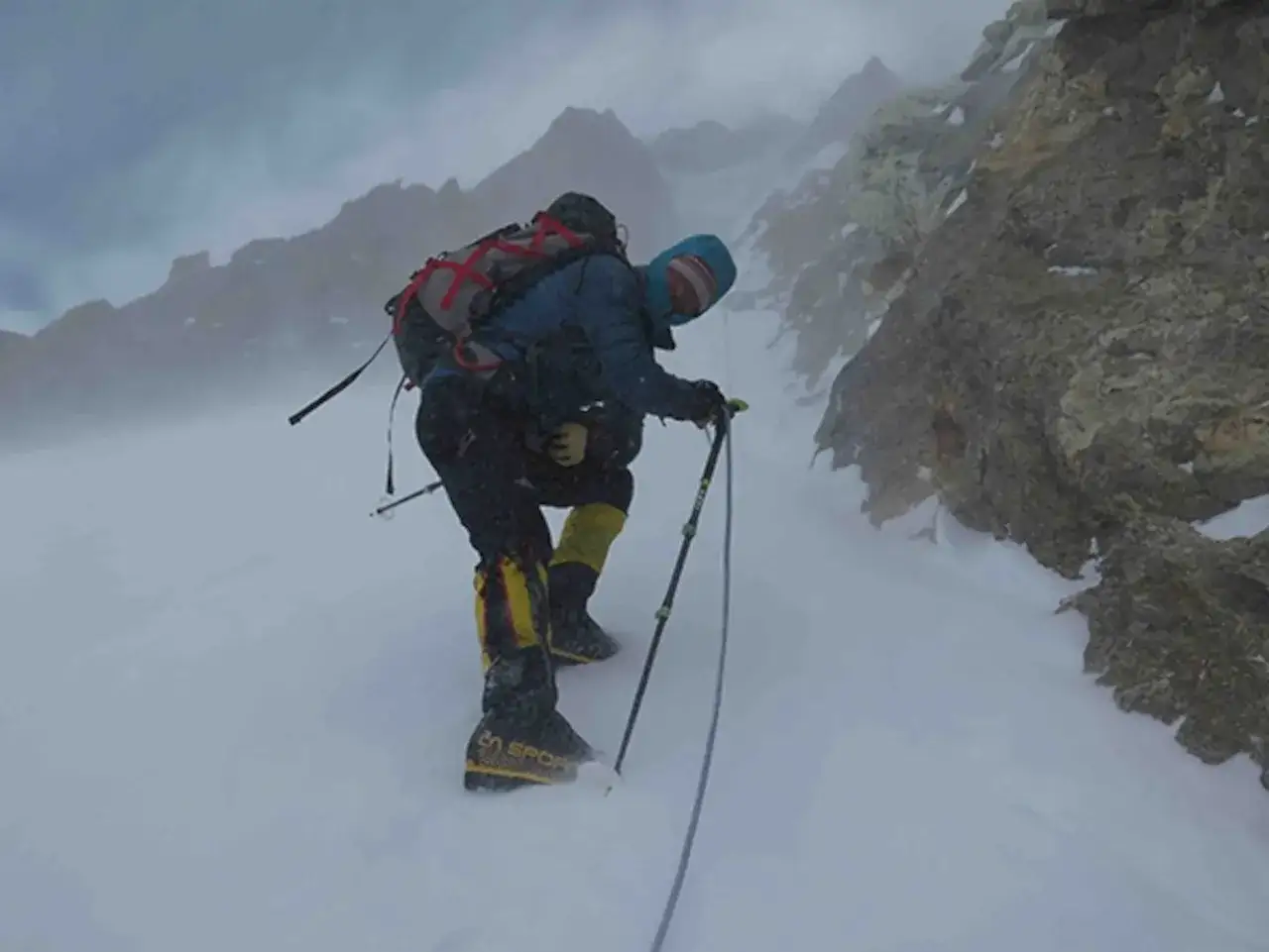 Bergsteiger Tomasz Mackiewicz k&auml;mpft sich durch eisigen Sturm und Schnee einen steilen, felsigen Hang hinauf.