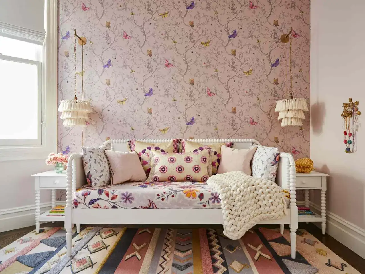 A white daybed styled with floral bedding and colorful pillows, featuring a chunky knit throw. This image shows how to style a daybed for a whimsical, butterfly-themed room.