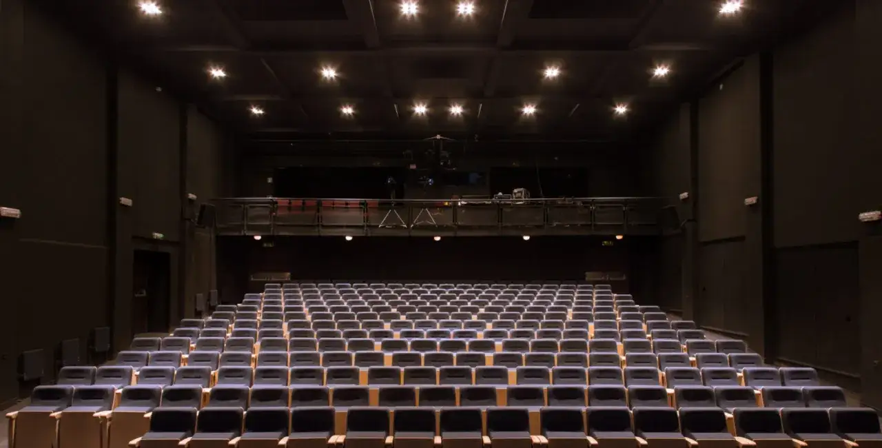 Puste rzędy siedzeń w **Teatrze Miejskim im. Witolda Gombrowicza** czekają na widzów. Wnętrze oświetlone jest punktowo z sufitu.