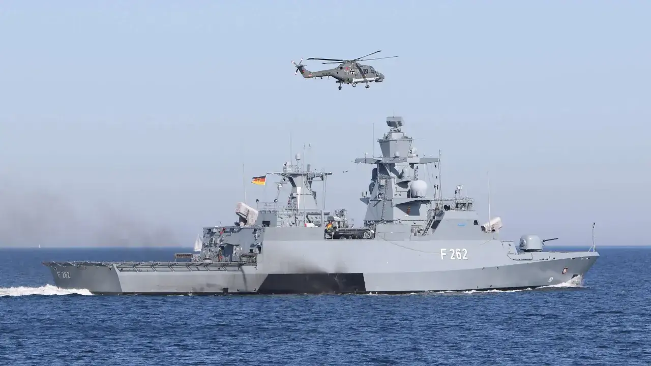 Ein deutsches Marinehubschrauber fliegt über der Fregatte F 262, einer modernen corvette ship, auf dem Meer.
