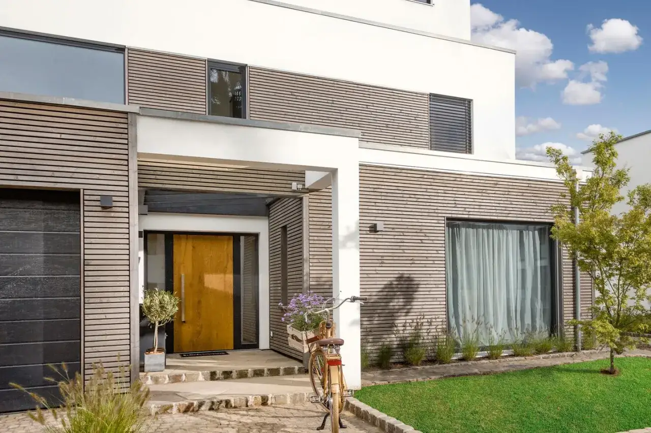 Ein moderner hauseingang gestalten: Holzfassade, große Glastür, Garage und ein Fahrrad mit Blumenkorb laden ein.