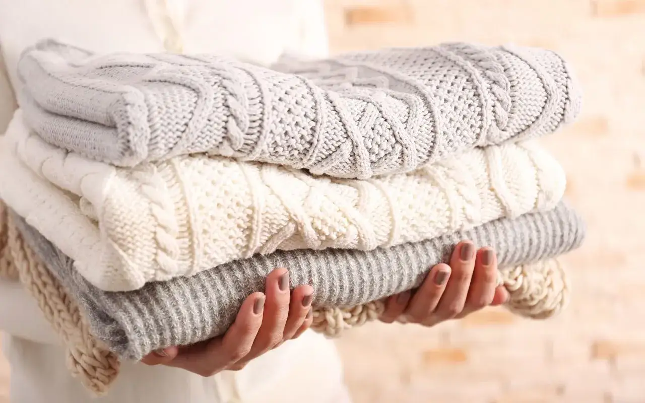 Pile de pulls en maille torsad&eacute;e gris et cr&egrave;me. Une astuce pour comment blanchir un pull blanc est de le laver avec ces couleurs claires.