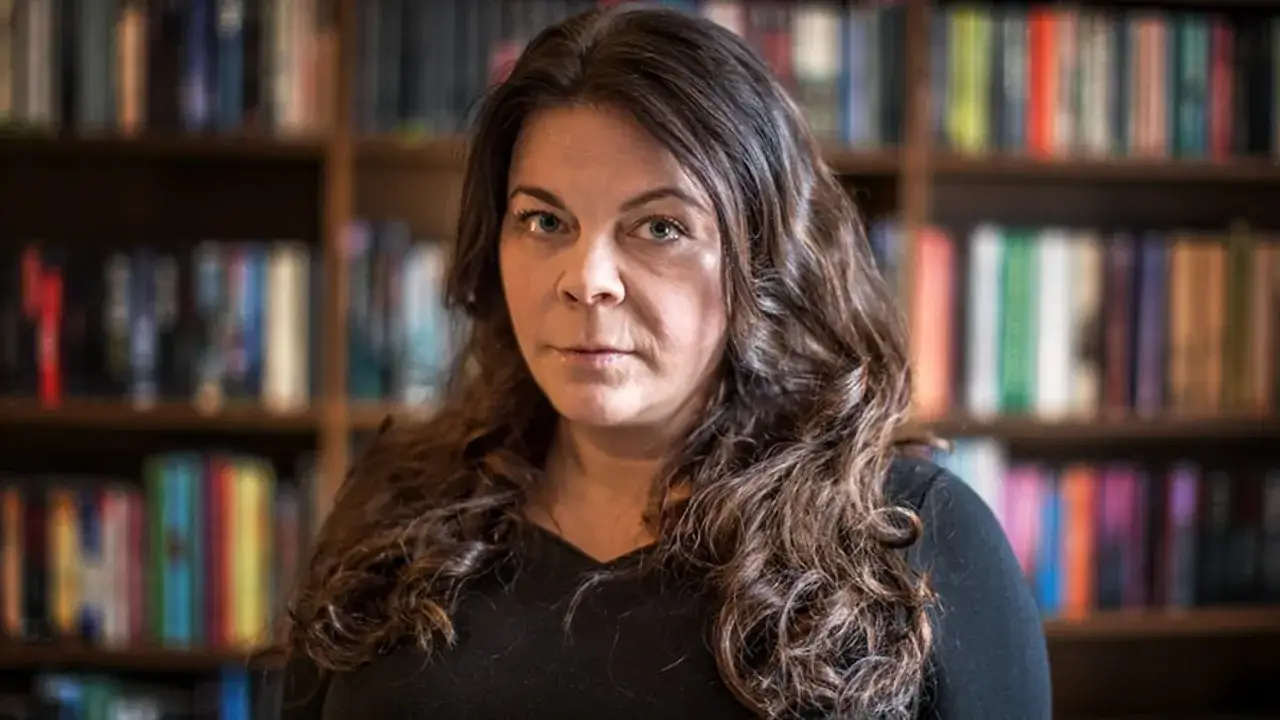 Jennifer Wegerup, med sitt lockiga h&aring;r, sitter framf&ouml;r en bokhylla fylld med b&ouml;cker.