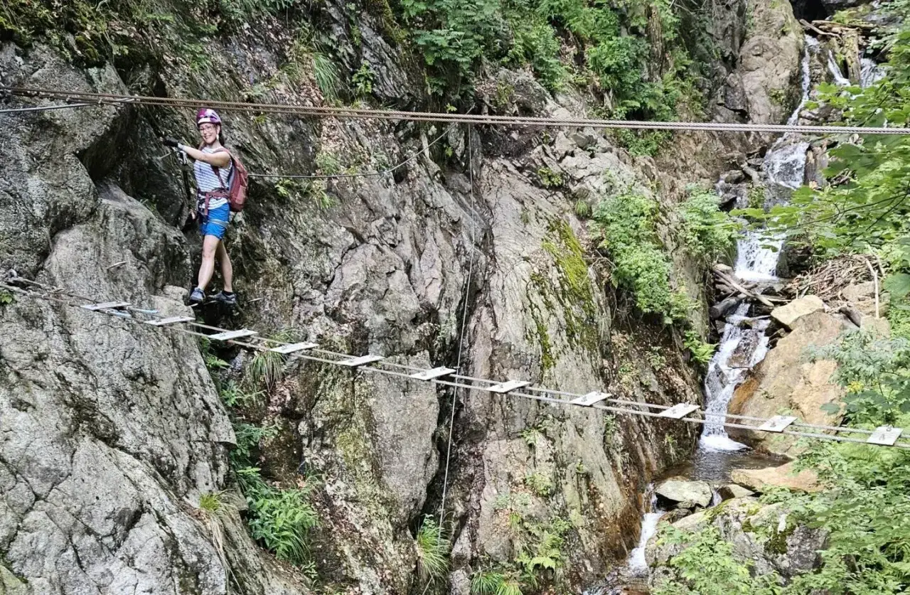 Kobieta na via ferrata polska pokonuje mostek nad wodospadem.